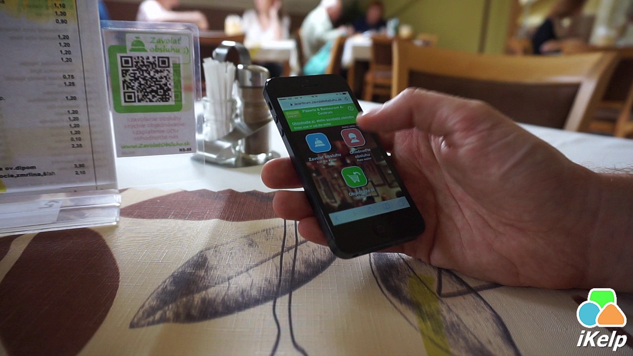 Hosť skenuje QR kód na stole, na obrazovke telefónu sa zobrazuje menu s možnosťami Zavolať obsluhu, Hodnotiť obsluhu a Objednávka